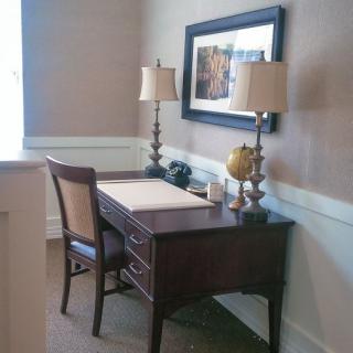 A cozy office corner with a wooden desk, chair, and lamps.