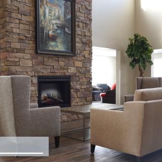 A cozy living room with a stone fireplace, armchairs, and a decorative painting.