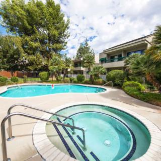 A scenic view of a residential outdoor area with a swimming pool and hot tub surrounded by lush greenery.