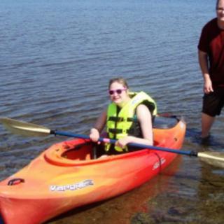 A person in a kayak wearing a life jacket with a paddle on a lake.