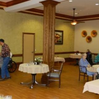 An interior view of a dining area in a nursing home with elderly residents seated at tables.