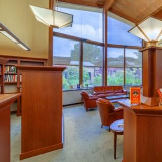 A cozy library with wooden furniture and large windows letting in natural light.