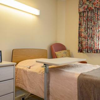 A hospital room with a bed and adjustable table next to a window with floral curtains.