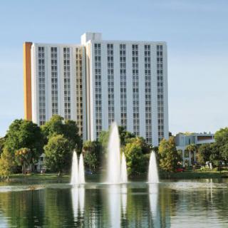 A high-rise building with fountains in a lake surrounded by trees.