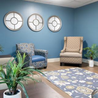 A cozy living room with blue walls, two armchairs, plants, and decorative mirrors.