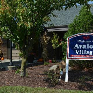 Entrance sign of Avalon Village with surrounding trees and landscaping.