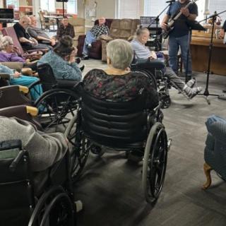 Elderly residents in wheelchairs enjoy a live music performance at a nursing home.