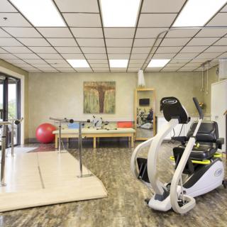 A well-equipped physical therapy room with various rehabilitation equipment, including a gym ball and parallel bars.
