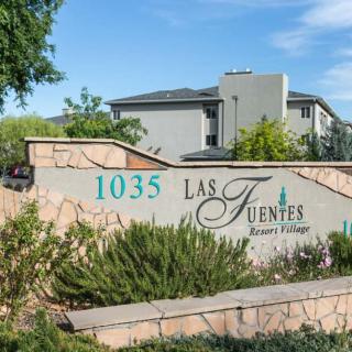 Entrance sign for Las Fuentes Resort Village, featuring landscaping and a view of residential buildings.
