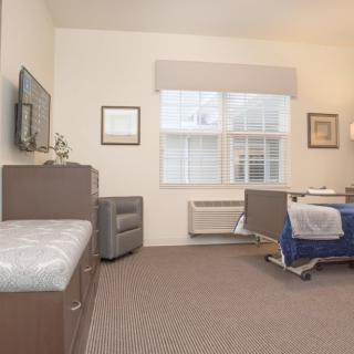 A hospital room with a bed, television, and window, featuring modern interior design.