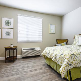 A cozy bedroom with a neatly made bed, artwork on the walls, and a wooden side table by the window.