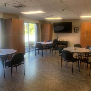 A spacious break room with round tables, chairs, and a wall-mounted television.