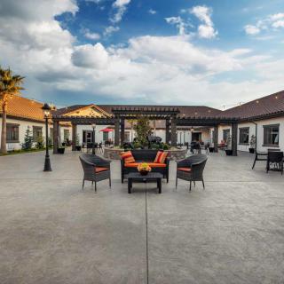 A modern outdoor patio with comfortable seating and decorative architecture under a partly cloudy sky.