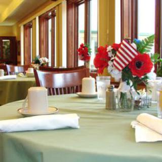 A restaurant dining area with tables set for guests, featuring floral arrangements and a small American flag.