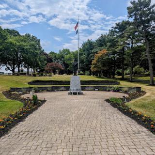 A serene park setting featuring a memorial monument surrounded by neatly arranged flower beds and a flagpole.