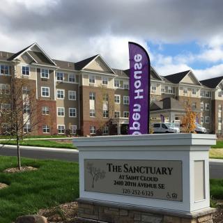 A modern apartment complex with a 'New Homes' banner displayed on a sunny day.