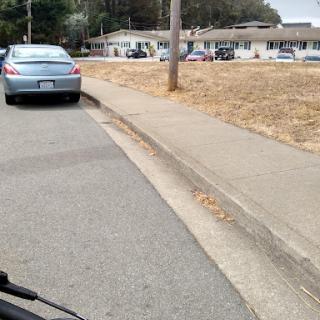 A view of a street with parked cars and a residential area in the background.
