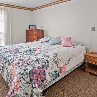 A cozy bedroom with a floral bedspread, wooden dresser, and nightstand.