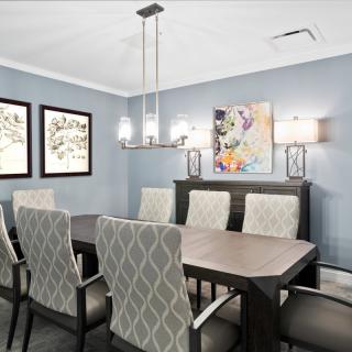 A modern dining room with a large table, patterned chairs, artwork on the walls, and a stylish chandelier.