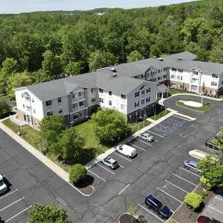 Aerial view of an apartment complex surrounded by trees with a parking lot in front.