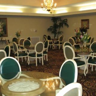 An elegant dining room with green cushioned chairs, round tables, and a chandelier.
