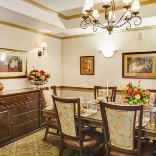A warmly decorated dining room with a wooden table and chairs, adorned with floral arrangements and artwork on the walls.