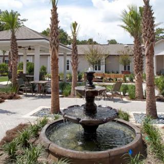 A serene courtyard featuring a multi-tiered fountain surrounded by palm trees and outdoor seating areas.