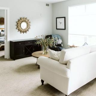 A bright and minimalist living room featuring a white sofa, wooden coffee table, and decorative mirror.