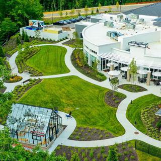An aerial view of a modern building surrounded by landscaped gardens and pathways, featuring a small greenhouse.