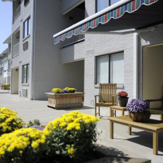 A sunny patio with outdoor seating and colorful flowers outside an apartment building.