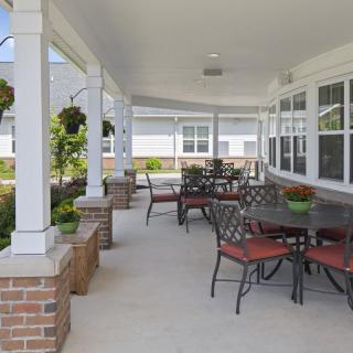 A spacious outdoor patio with tables and chairs under a covered area, featuring hanging plants and brick accents.