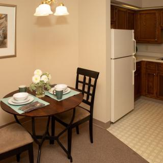 A cozy dining area adjacent to a small kitchen, featuring a table set for two and wooden cabinetry.