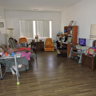 A cozy living room featuring comfortable chairs, a computer setup, and wooden flooring bathed in natural light.