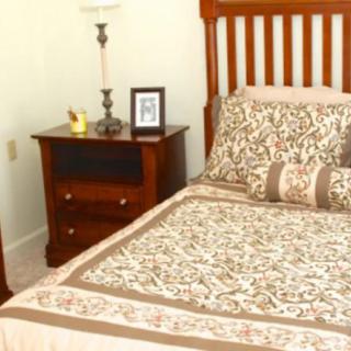 A neatly arranged bedroom with a wooden bed frame, patterned bedding, and a nightstand featuring a lamp and framed photo.