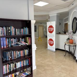 A cozy library corner featuring a bookshelf filled with books, a welcoming waiting area, and informational banners.