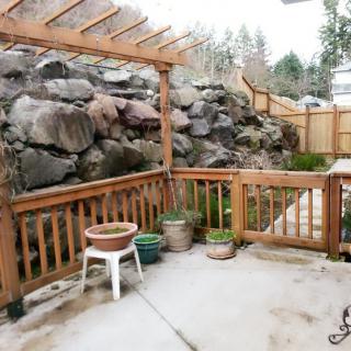 A cozy patio area with wooden fencing, potted plants, and a rock wall backdrop.