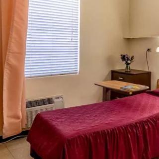 A simple bedroom with a single bed, nightstand, and window with blinds.