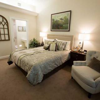 A cozy bedroom with a neatly made bed, armchair, and warm lighting.