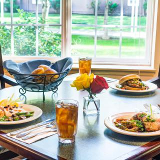A beautifully set dining table with delicious meals and refreshing drinks near a sunny window.
