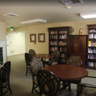 A quiet library room with round tables, chairs, and bookshelves filled with books.