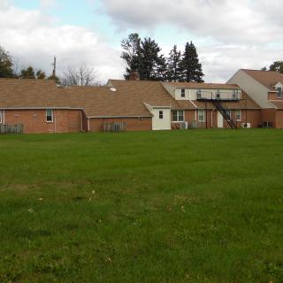 A view of a residential complex with a large grassy field and cloudy sky.