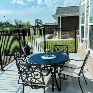 An outdoor patio with a round table and four chairs, enclosed by a metal fence, overlooking a garden.