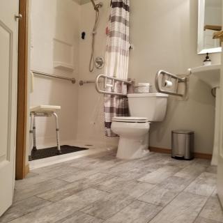 A modern, accessible bathroom featuring a shower with grab bars, toilet, and sink.