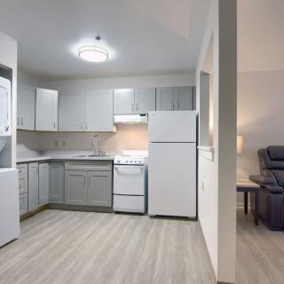 Modern apartment kitchen with light wood flooring and white cabinetry.