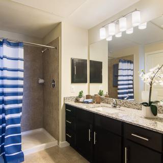 A modern bathroom with a striped blue shower curtain, double sink vanity, and elegant lighting.
