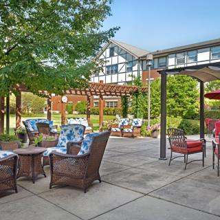A cozy outdoor patio with comfortable furniture and a pergola surrounded by lush greenery.
