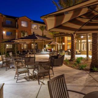 A well-lit outdoor patio with tables and chairs set under umbrellas by a building in the evening.