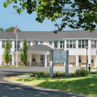 A hospital building with an American flag, surrounded by trees and a sunny sky.