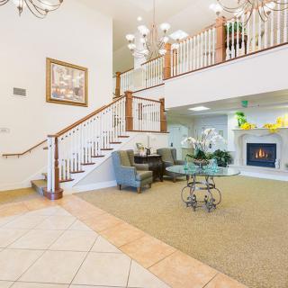 A spacious living room featuring a grand staircase, elegant chandelier, and cozy seating area by the fireplace.