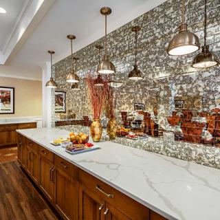 A modern kitchen with a marble island, pendant lighting, and a reflective backsplash.